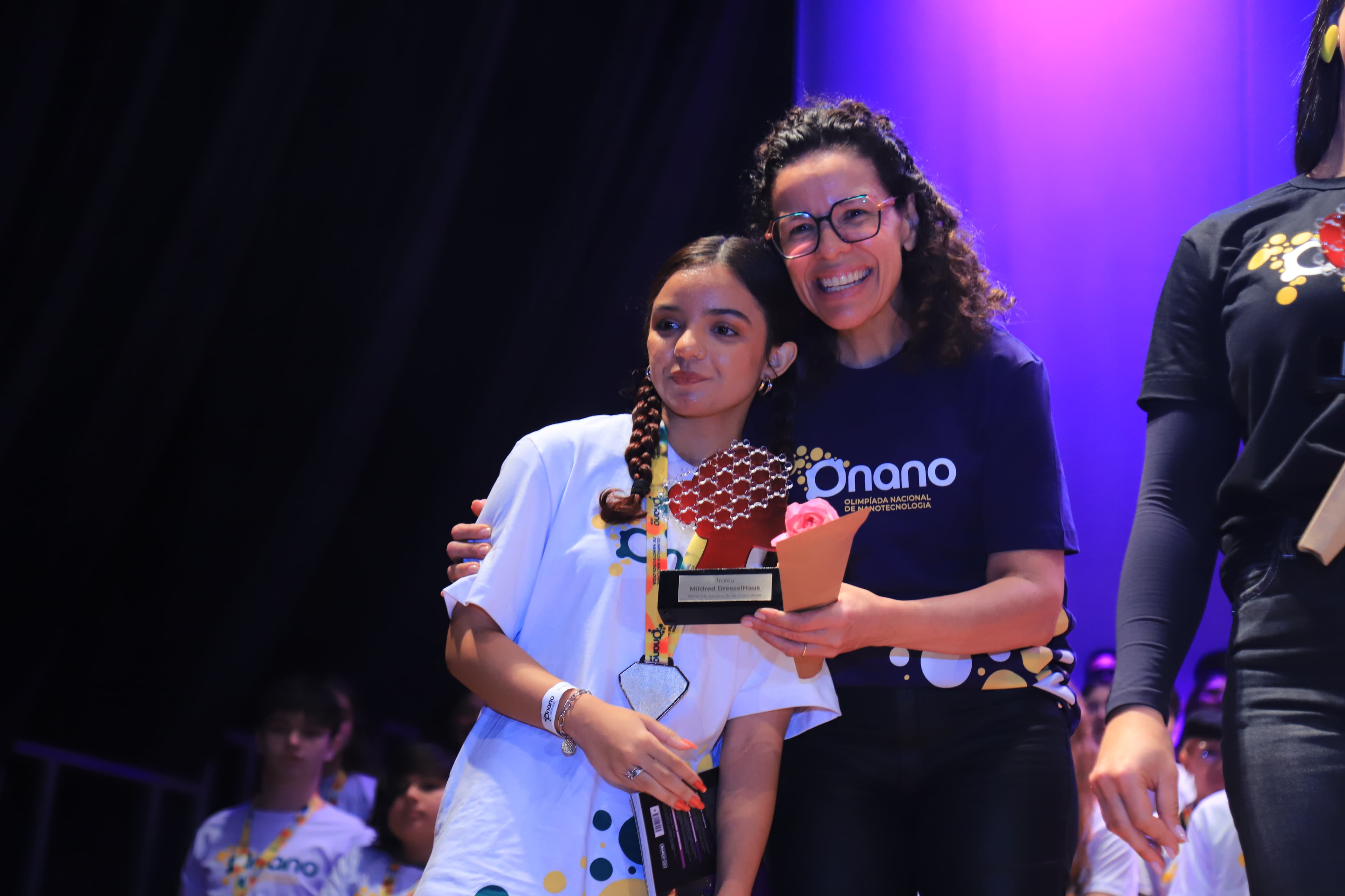 Medalhista abraçada com organizadora no palco da premiação da ONANO
